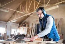 نجار يعمل في ورشة خشبية يرتدي سماعات حماية.