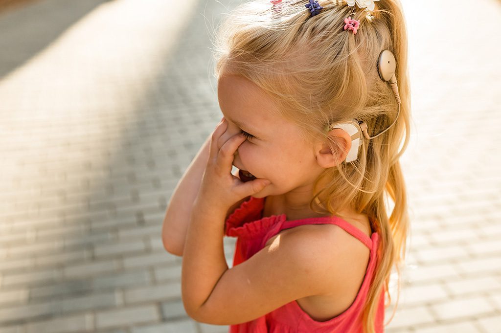 Enfant souriant portant un appareil auditif.