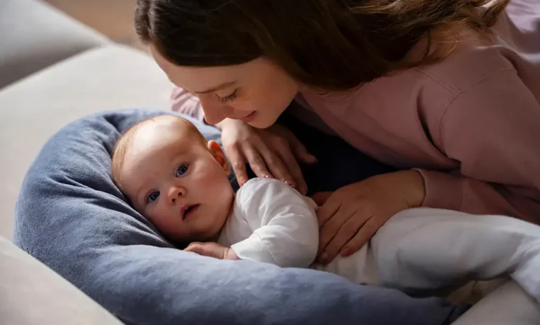 Mère souriante regardant bébé sur oreiller bleu.