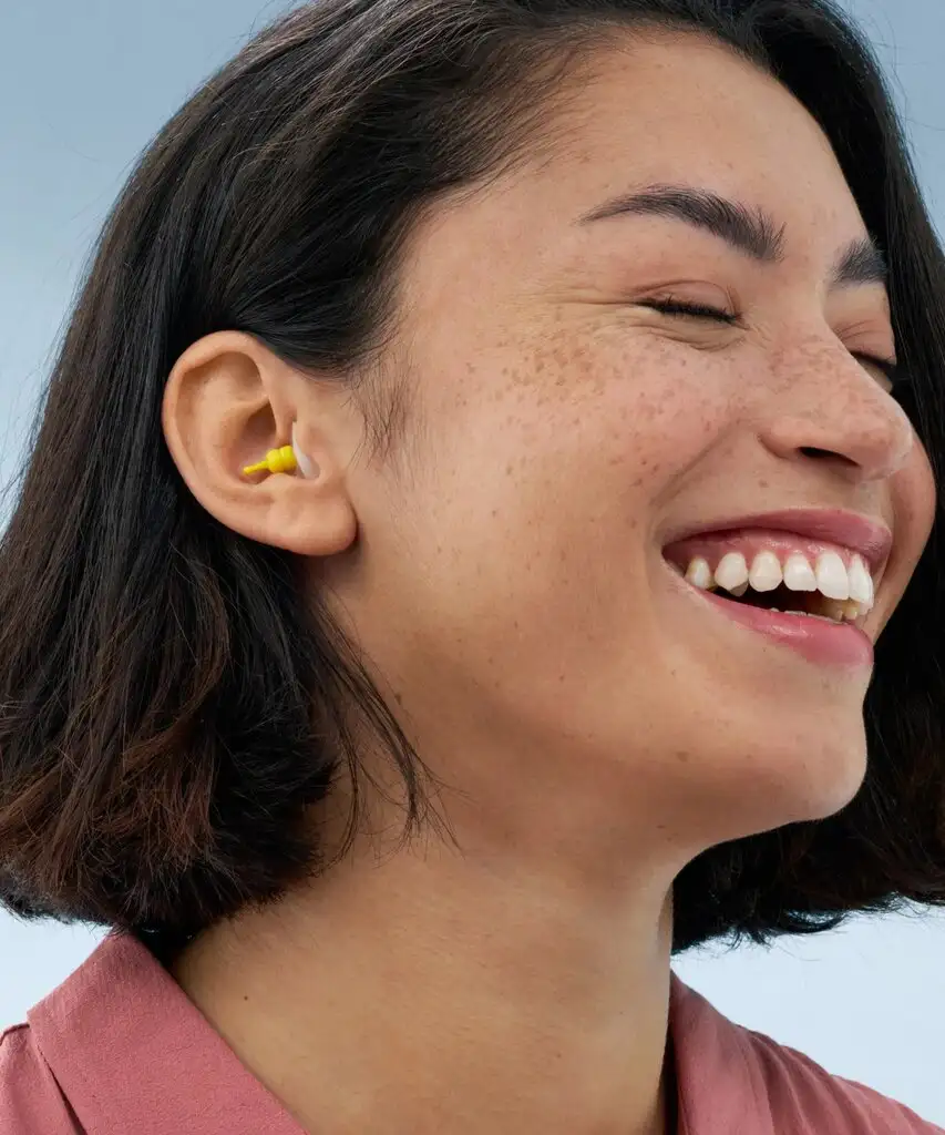 Femme souriante avec des bouchons d'oreilles jaunes.