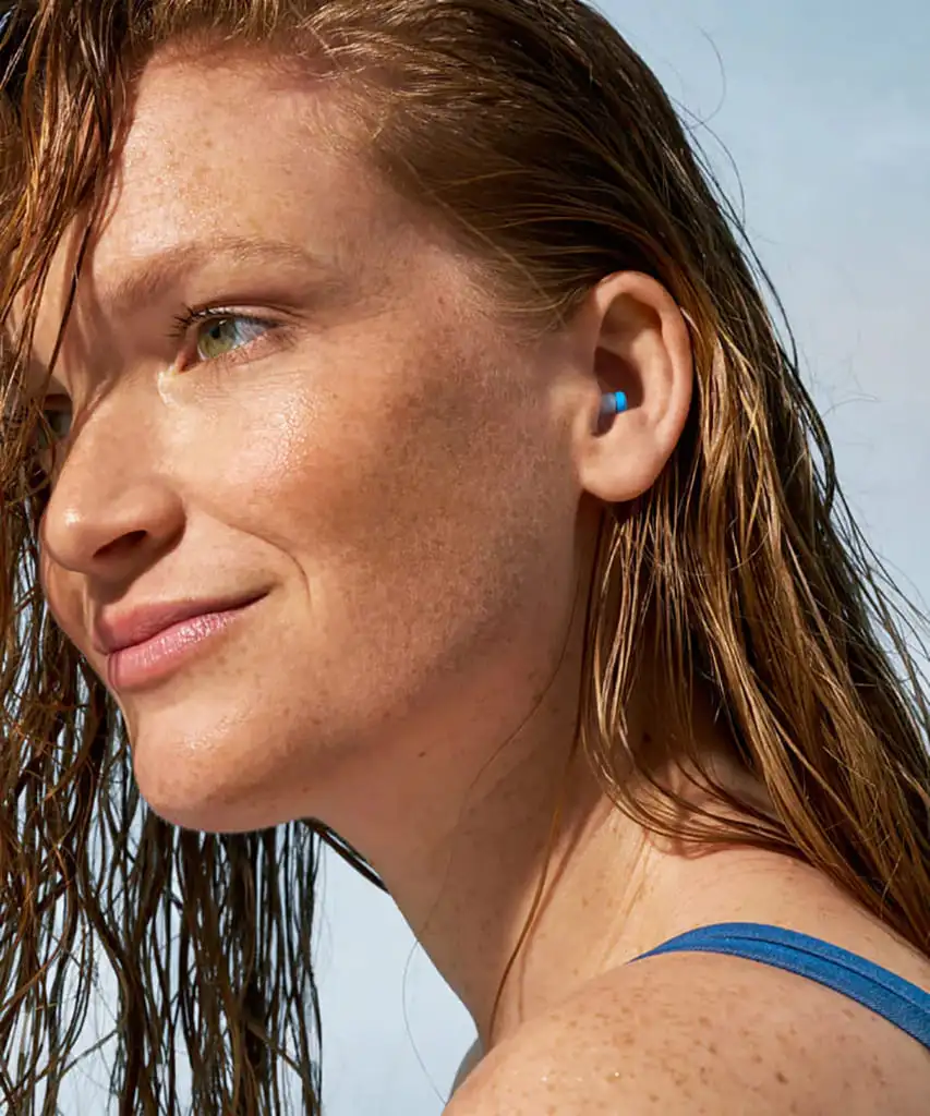 Femme avec écouteurs intra-auriculaires bleus, cheveux mouillés.